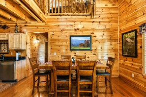Ein Holzblockhaus-Innenraum mit Esstisch, Stühlen, einer Küchenzeile und einem gerahmten Bild an der Wand.