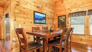 Een houten hut interieur met een eettafel, stoelen, een televisie en ingelijste foto's aan de muren.