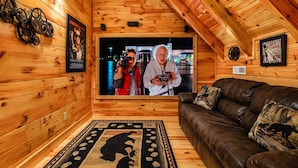 Een gezellig interieur van een chalet met houten accenten, een leren bank, een vloerkleed met dessin en een groot schilderij in een lijst aan de muur.