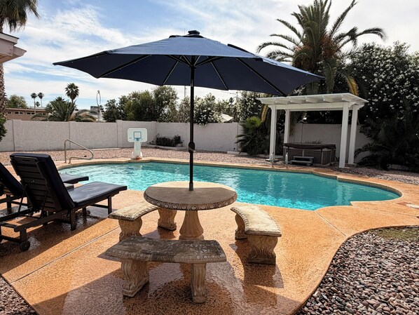A swimming pool with lounge chairs, a table, and an umbrella.
