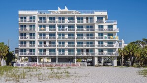 Un hotel de varios pisos con balcones, situado en una playa con arena en primer plano.
