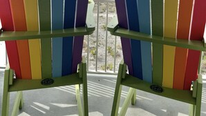 Dos sillas Adirondack coloridas mirando una playa con vista al océano y un cielo despejado.