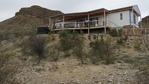 Ein zweistöckiges Haus mit Balkon, umgeben von Wüstenpflanzen und einem Berg im Hintergrund.