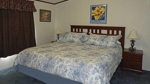 Ein Schlafzimmer mit einem Bett, zwei Nachttischen, einem Fenster mit Vorhängen und einem an der Wand hängenden Bild.