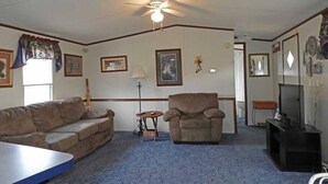 Ein Wohnzimmer mit Deckenventilator, einer Couch, einem Sessel, einem kleinen Tisch und einem Fernseher.