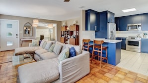 A modern living room with a large L-shaped sofa, a glass coffee table, and a dining area with bar stools. The kitchen features dark blue cabinets, stainless steel appliances, and a white countertop. - Heated Private Pool - Bring your Kayak  (Savannah)