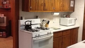 A kitchen with wooden cabinets, a gas stove, an oven, a microwave, and a countertop with kitchen utensils. - 3 Bedroom, Cozy Cottage Near Seney Wildlife Refuge (Seney)
