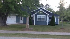 A single-story house with a garage, a front yard with a small tree, and a driveway. - 3 Bedroom, Cozy Cottage Near Seney Wildlife Refuge (Seney)