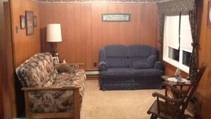 A living room with a patterned sofa, a blue couch, a wooden rocking chair, and a lamp. - 3 Bedroom, Cozy Cottage Near Seney Wildlife Refuge (Seney)
