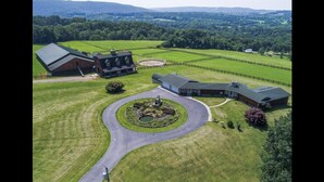 An aerial view of a property with a large barn, a guesthouse, and a circular driveway leading to a landscaped area with a pond. - Nunda Ranch near Letchworth State Park (Nunda)