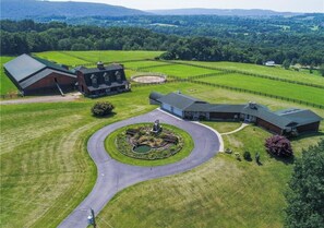 An aerial view of a property with a large barn, a guesthouse, and a circular driveway leading to a landscaped area with a pond. - Nunda Ranch near Letchworth State Park (Nunda)