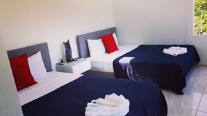 A hotel room with two beds, each with a red pillow and a white pillow, and a small nightstand with a lamp and a decorative item. - House of Views (La Fortuna)