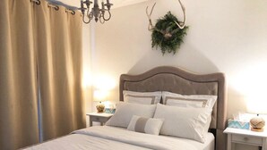 A neatly made bed with a patterned bedspread, a headboard with decorative pillows, a wall-mounted plant, and a chandelier.