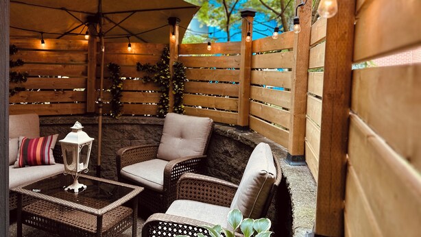 An outdoor patio with wicker furniture, a glass table, and a lantern.
