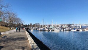 A marina with boats docked, a pedestrian path, and a bridge in the background.