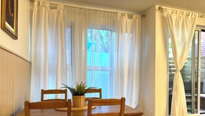 A dining area with a wooden table and chairs, a woven basket with a plant, and sheer curtains.