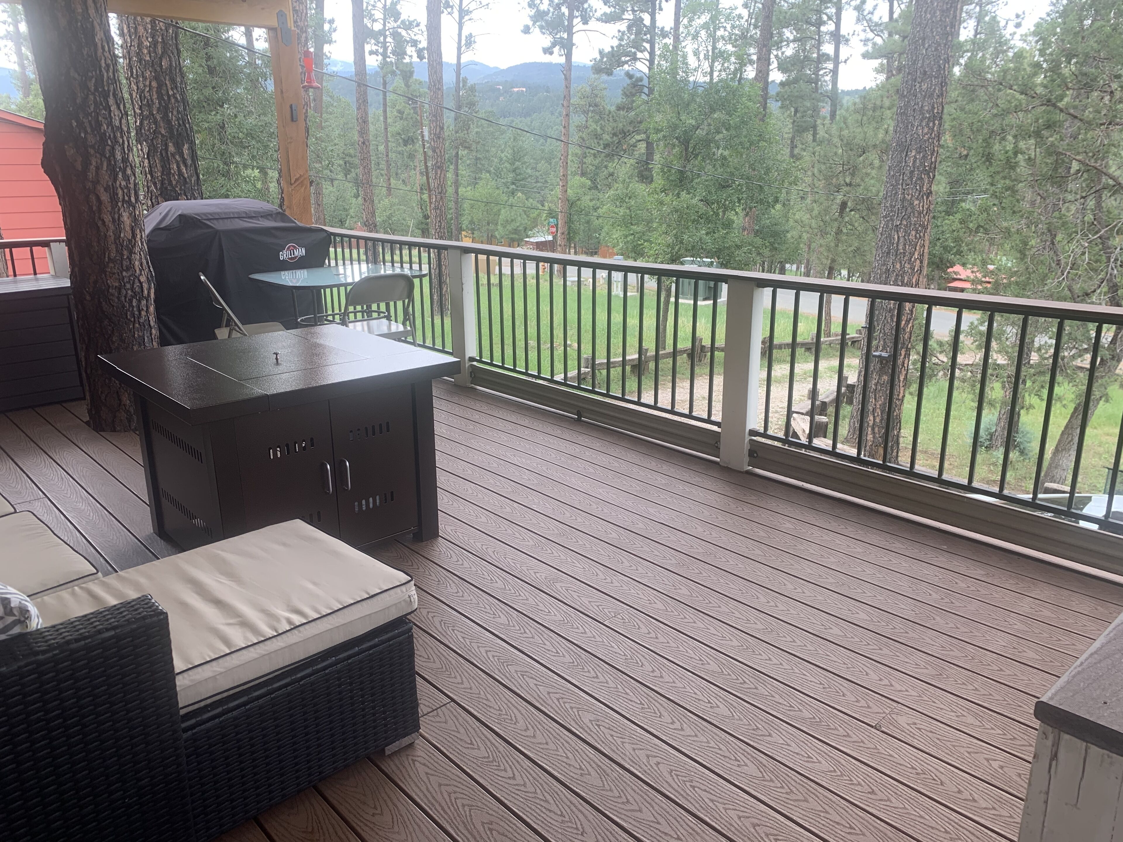 A covered outdoor deck with a grill, wicker furniture, and a view of a forested area.