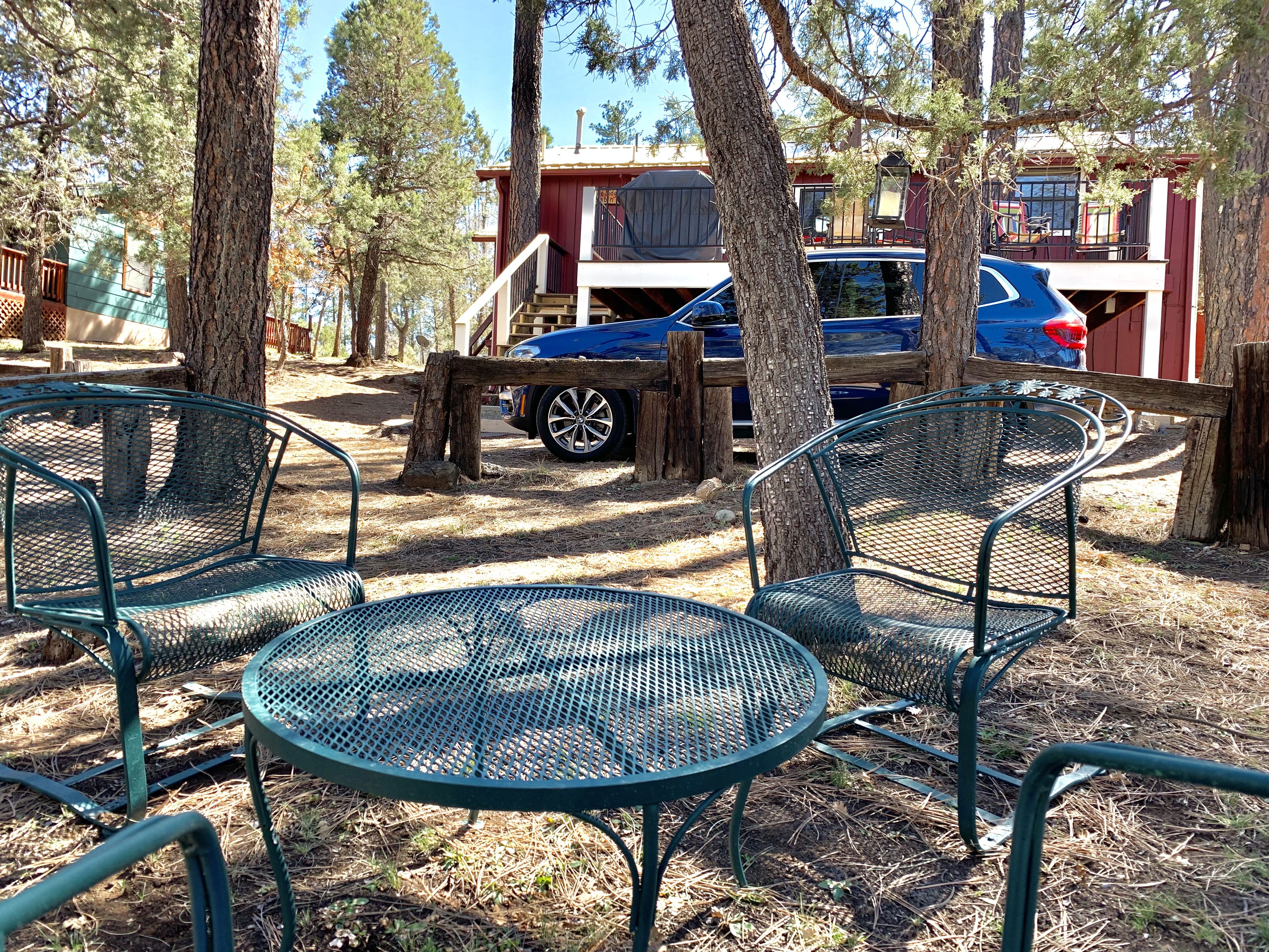 A rustic outdoor seating area with metal tables and chairs, surrounded by trees and a wooden fence.