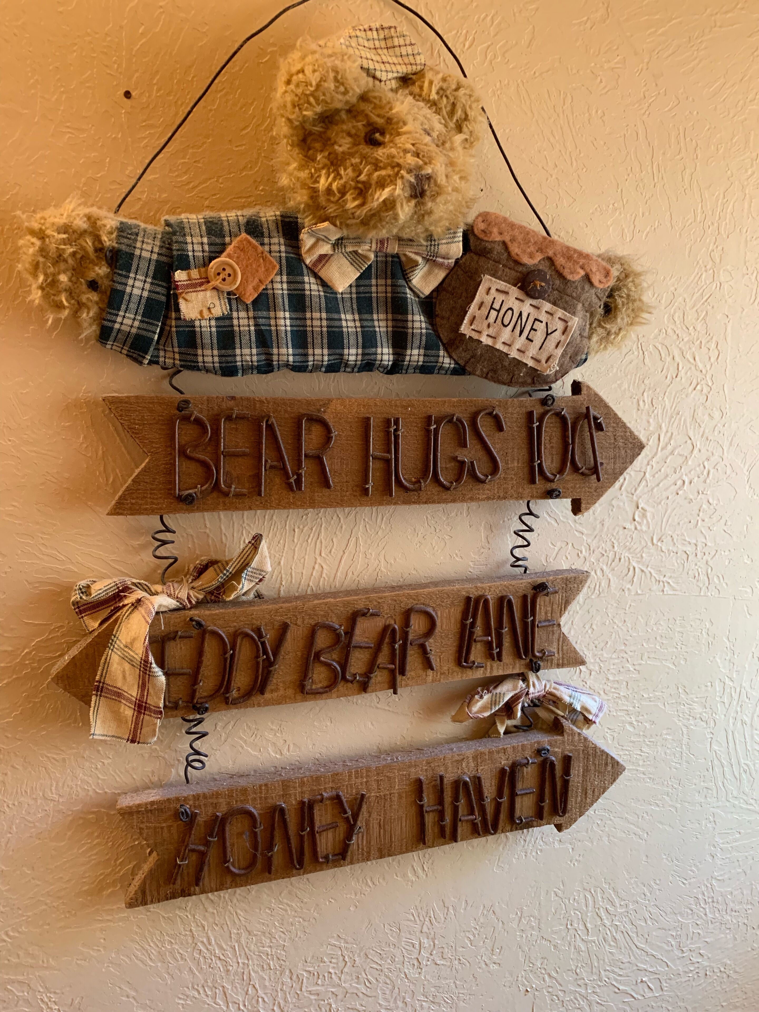 Decoración de pared con un osito de peluche, tela escocesa y letreros de madera con texto.