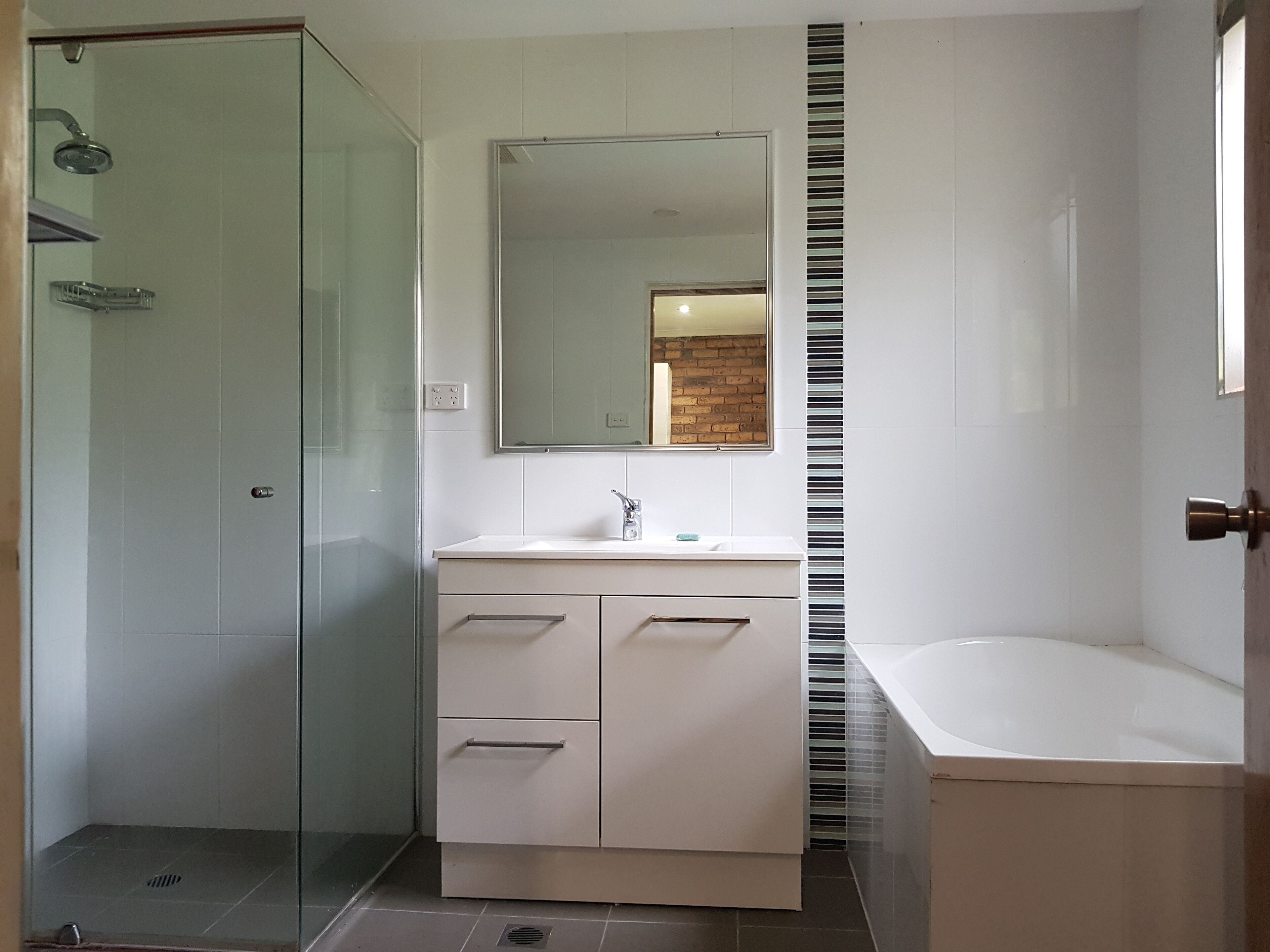 Een moderne badkamer met een douchecabine van glas, een witte wastafel met spiegel en een apart badgedeelte.