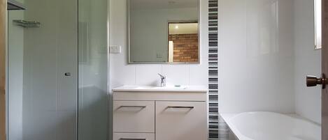 Een moderne badkamer met een douchecabine van glas, een witte wastafel met spiegel en een apart badgedeelte.