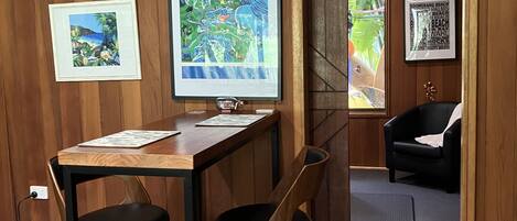 A room with a wooden paneled wall, a desk with two chairs, a framed map, and a black leather chair.