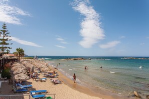 A beach with clear skies, palm trees, and thatched umbrellas.