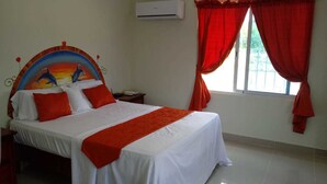 A hotel room with a bed, a nightstand, a wall-mounted air conditioner, and a window with red curtains.