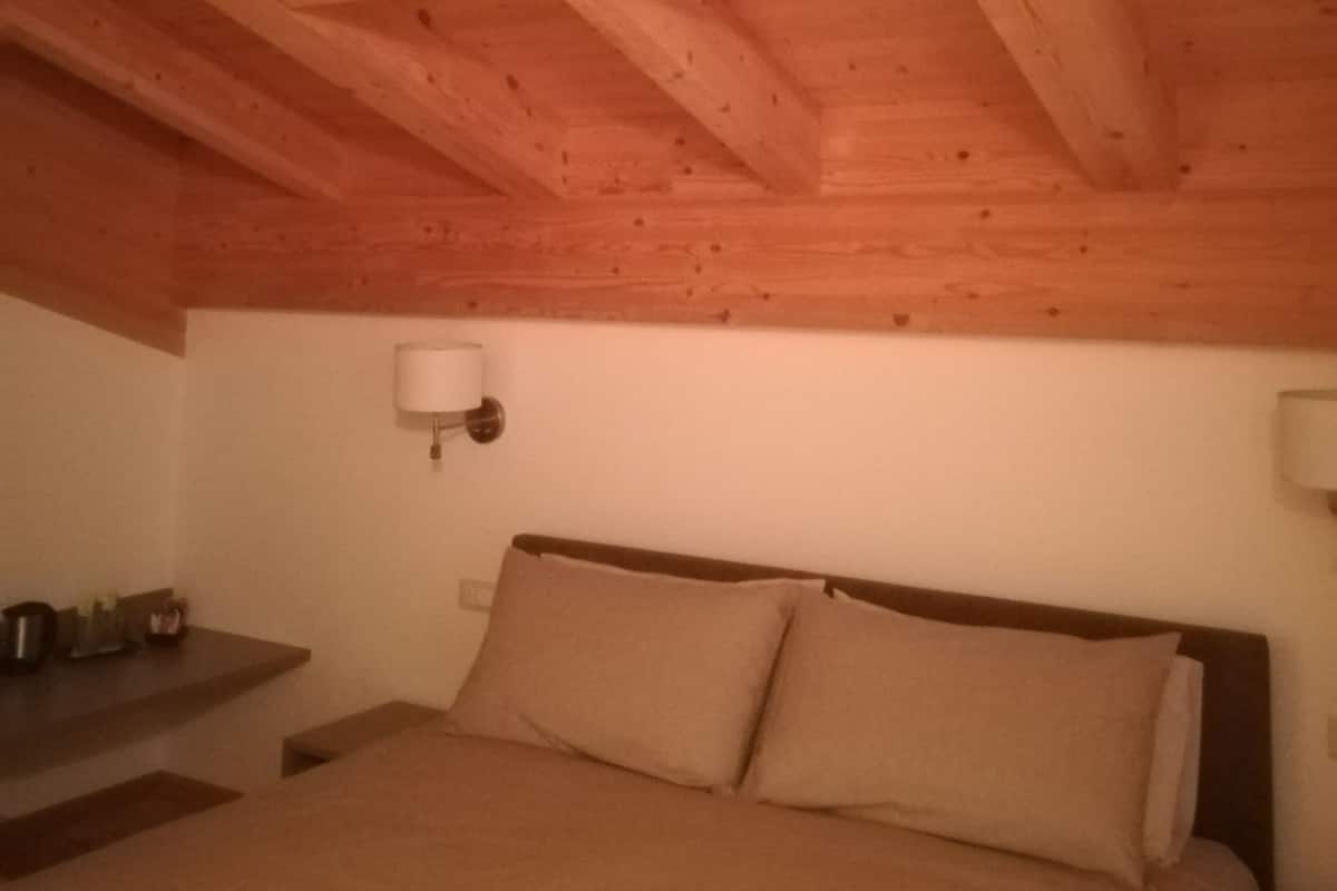 Un dormitorio con techo de madera, una cama con dos almohadas, una mesita de noche y una lámpara de pared.