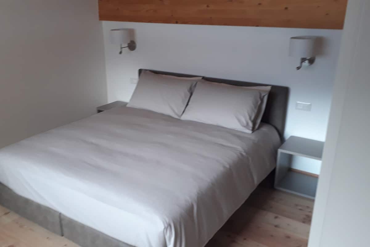 Un dormitorio con cama, mesitas de noche e iluminación en la pared.