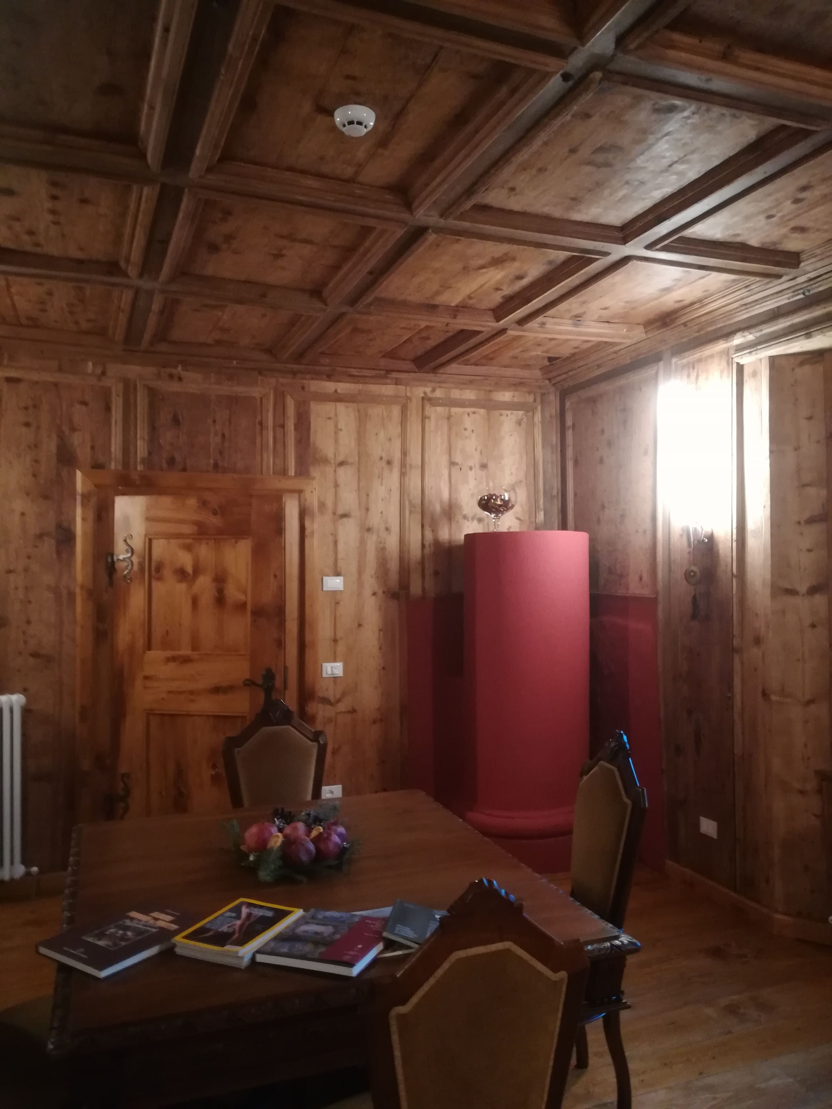 A wooden-paneled room with a dining table, chairs, and a red pillar.