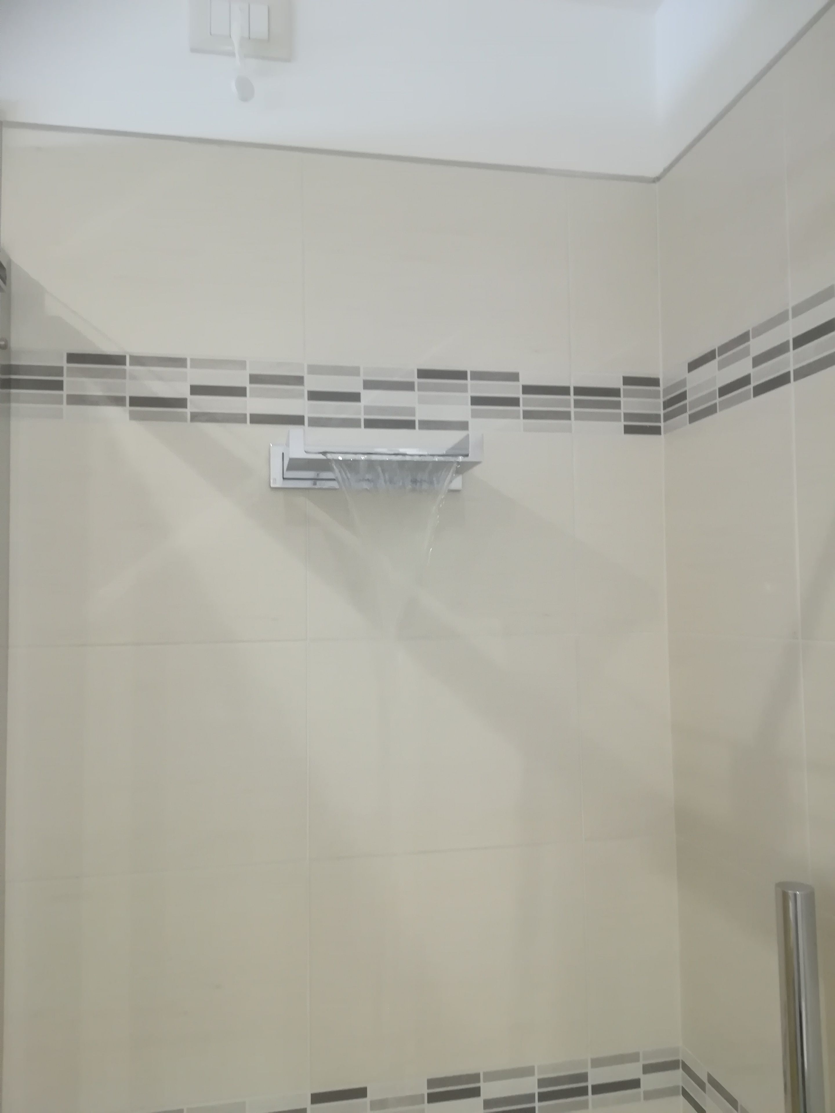 A bathroom with a shower area, a towel rack, and a tiled wall with a decorative border.