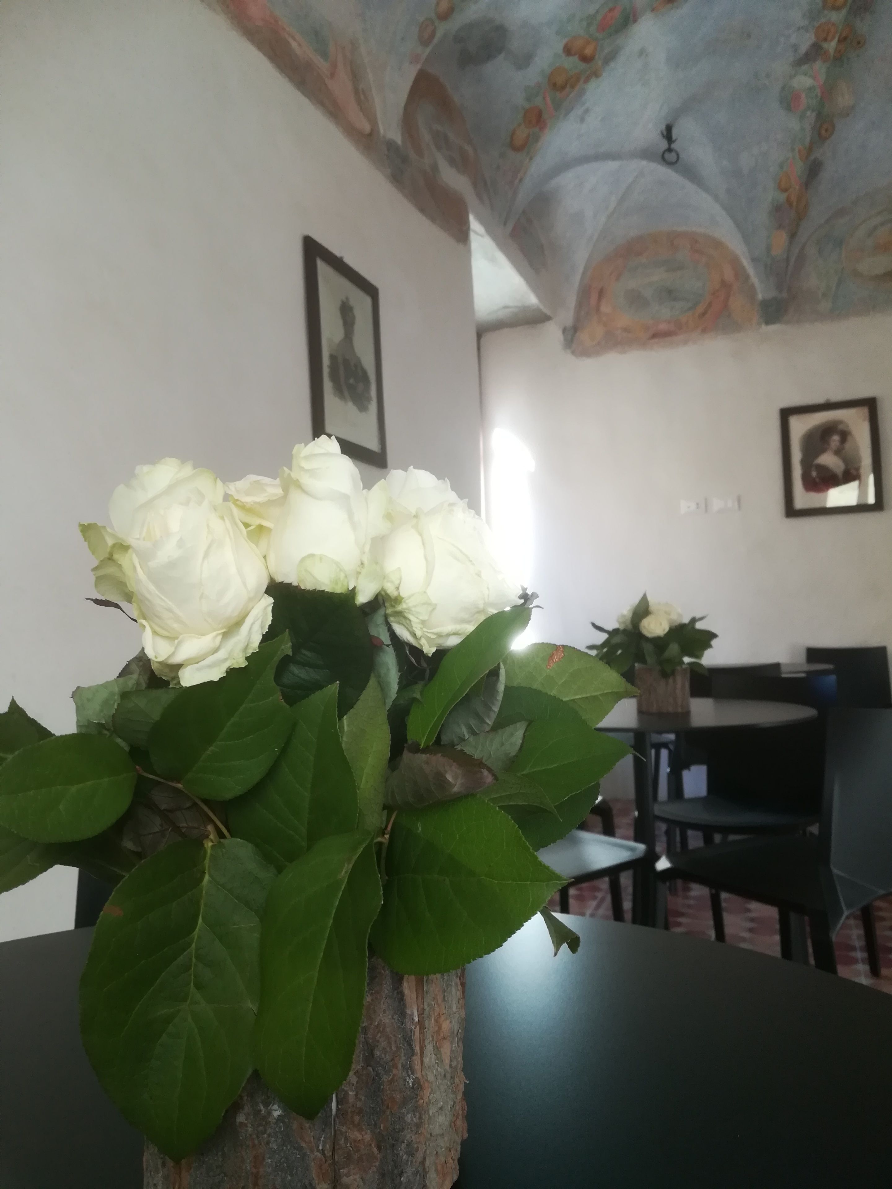 Ein Essbereich mit Tisch und Stühlen, einer Vase mit weißen Rosen und einer Decke mit Fresken.