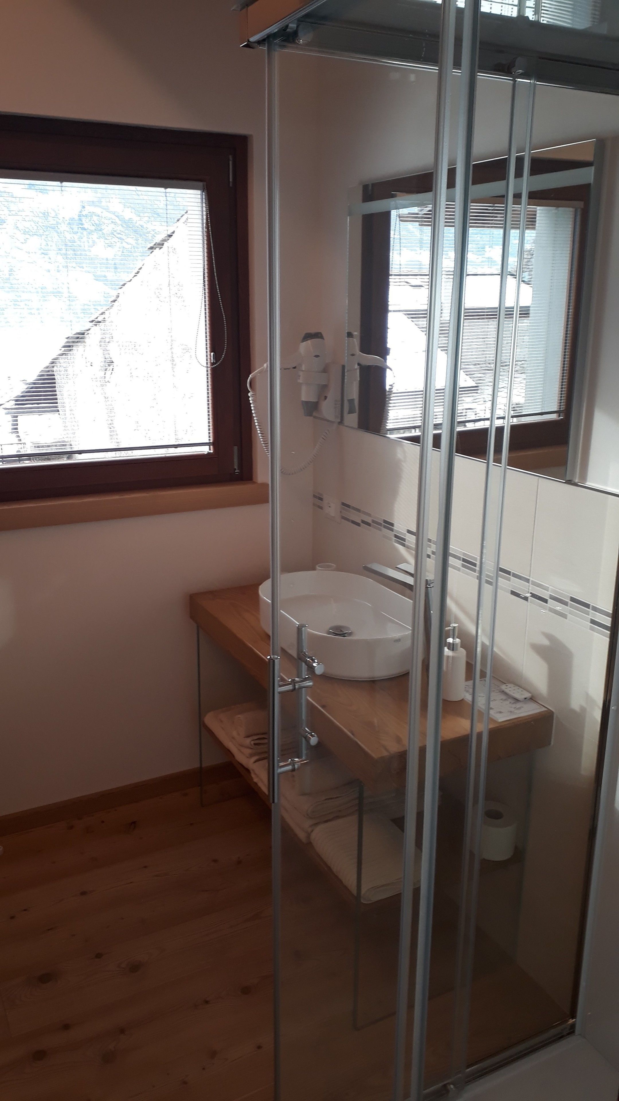 A bathroom with a wooden vanity, a white sink, and a glass-enclosed shower area.
