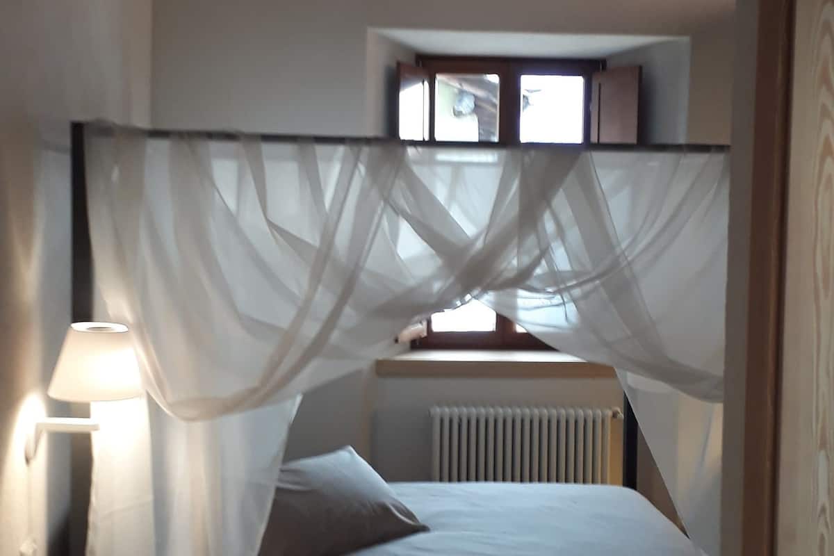Un dormitorio con cama, mesita de noche, lámpara, ventana con cortinas y radiador.