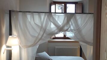 Une chambre à coucher avec un lit, une table de chevet, une lampe, une fenêtre avec des rideaux et un radiateur.