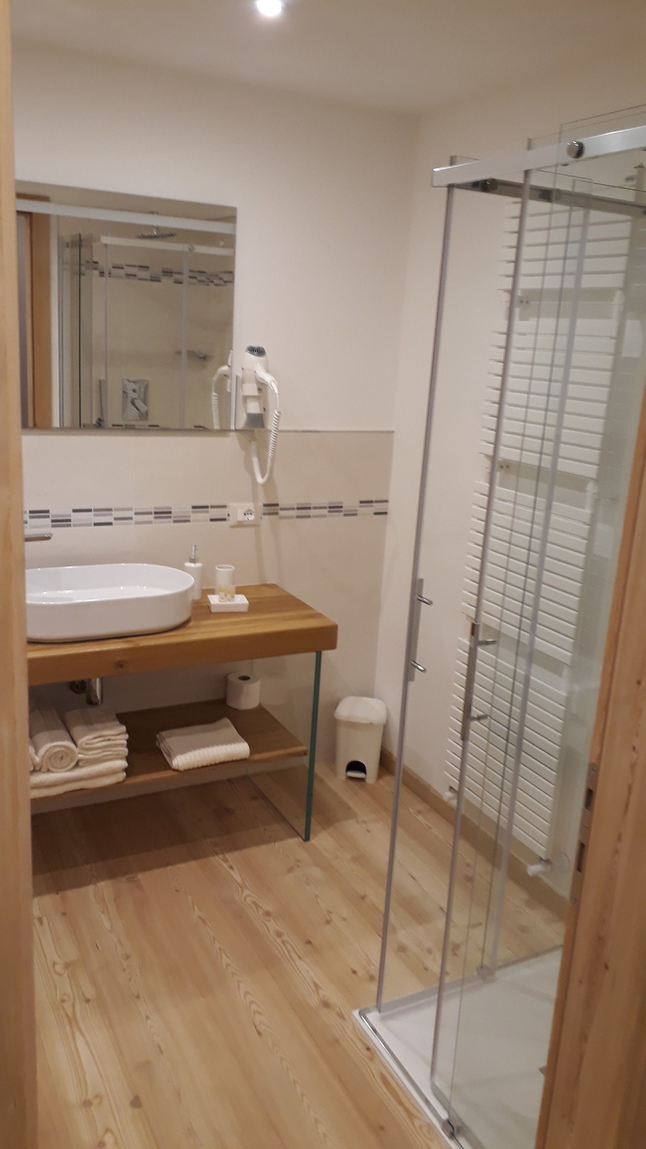 Une salle de bain avec un meuble-lavabo en bois, un lavabo blanc, un miroir, une cabine de douche en verre et des toilettes.
