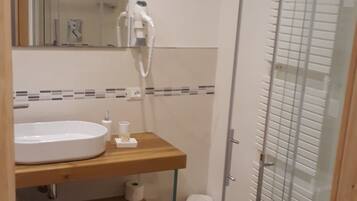 Une salle de bain avec un meuble-lavabo en bois, un lavabo blanc, un miroir, une cabine de douche en verre et des toilettes.