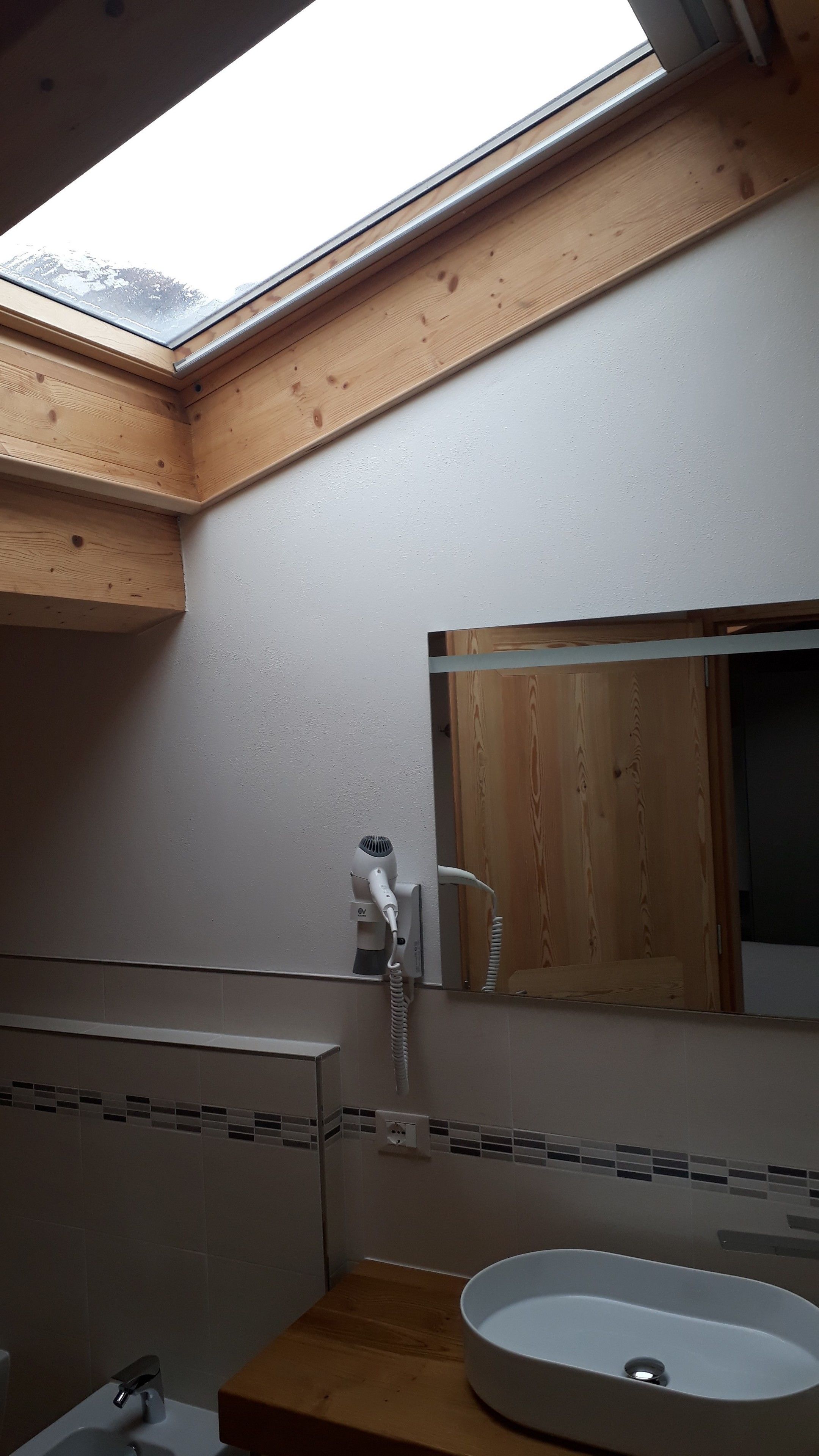 A bathroom with a skylight, a wooden vanity, a sink, and a mirror.