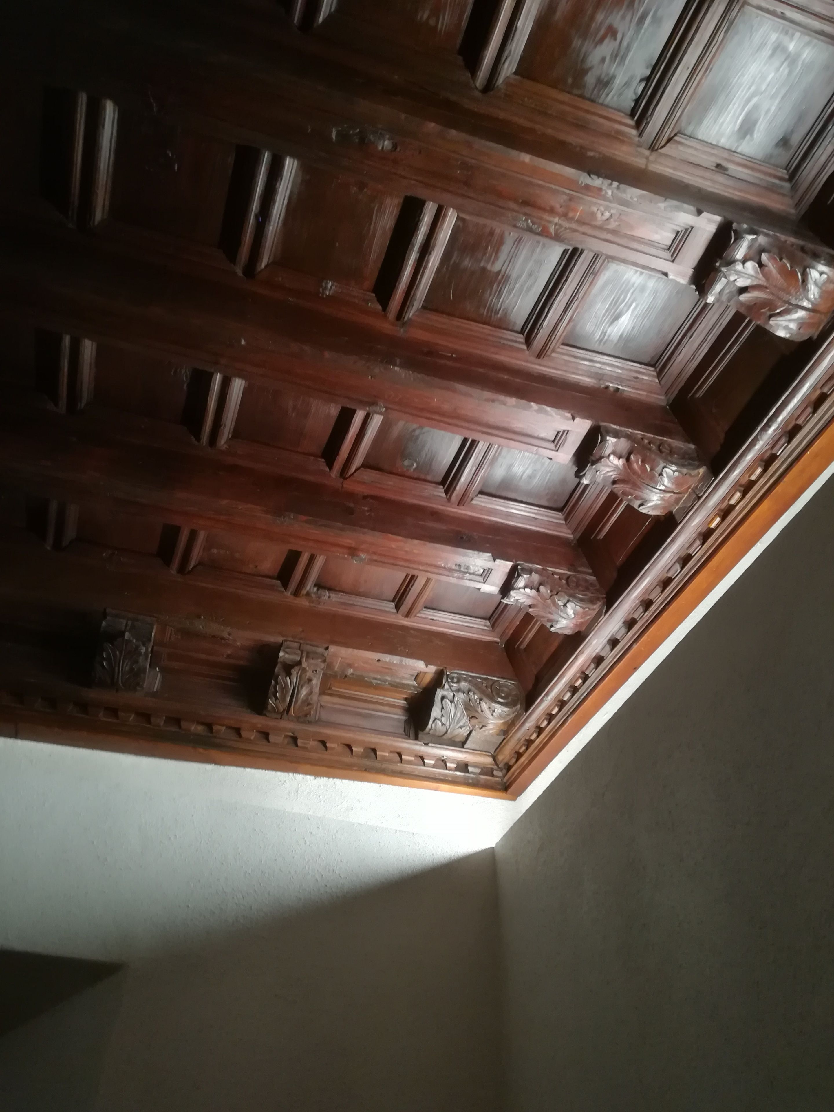 A wooden ceiling with intricate carvings and a corner of a room with a white wall.