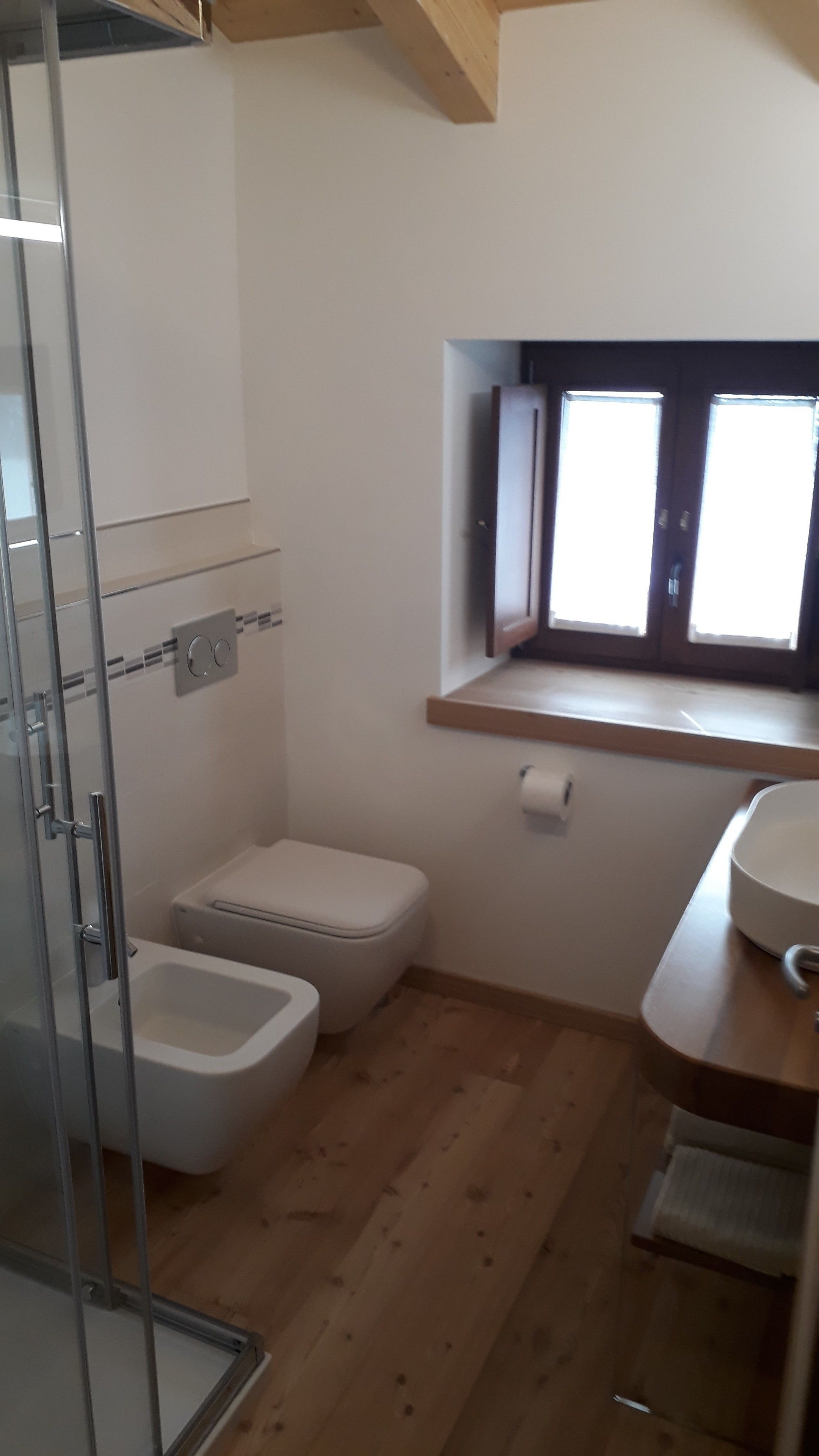 A small, compact bathroom with a glass shower enclosure, a toilet, and a sink with a wooden countertop.