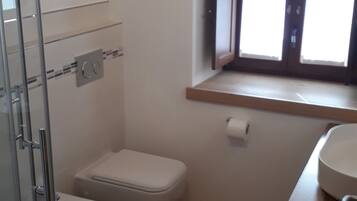 Une petite salle de bain compacte dotée d’une douche en verre, de toilettes et d’un lavabo avec un plan de travail en bois.