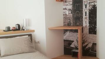A bedroom with a bed, a wooden desk, a hanging light fixture, and a wall-mounted coat rack.