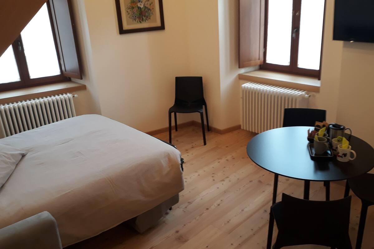 Una habitación con cama, una mesa con sillas, un radiador y una ventana.