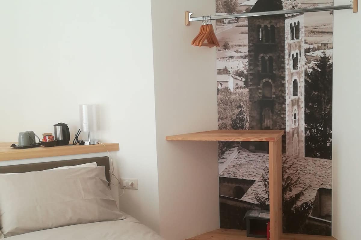 Un dormitorio con cama, escritorio de madera, lámpara colgante y perchero en la pared.