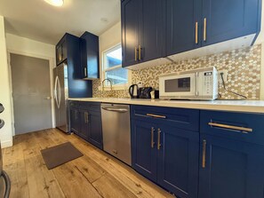 A modern kitchen with dark blue cabinets, stainless steel appliances, and a patterned backsplash.