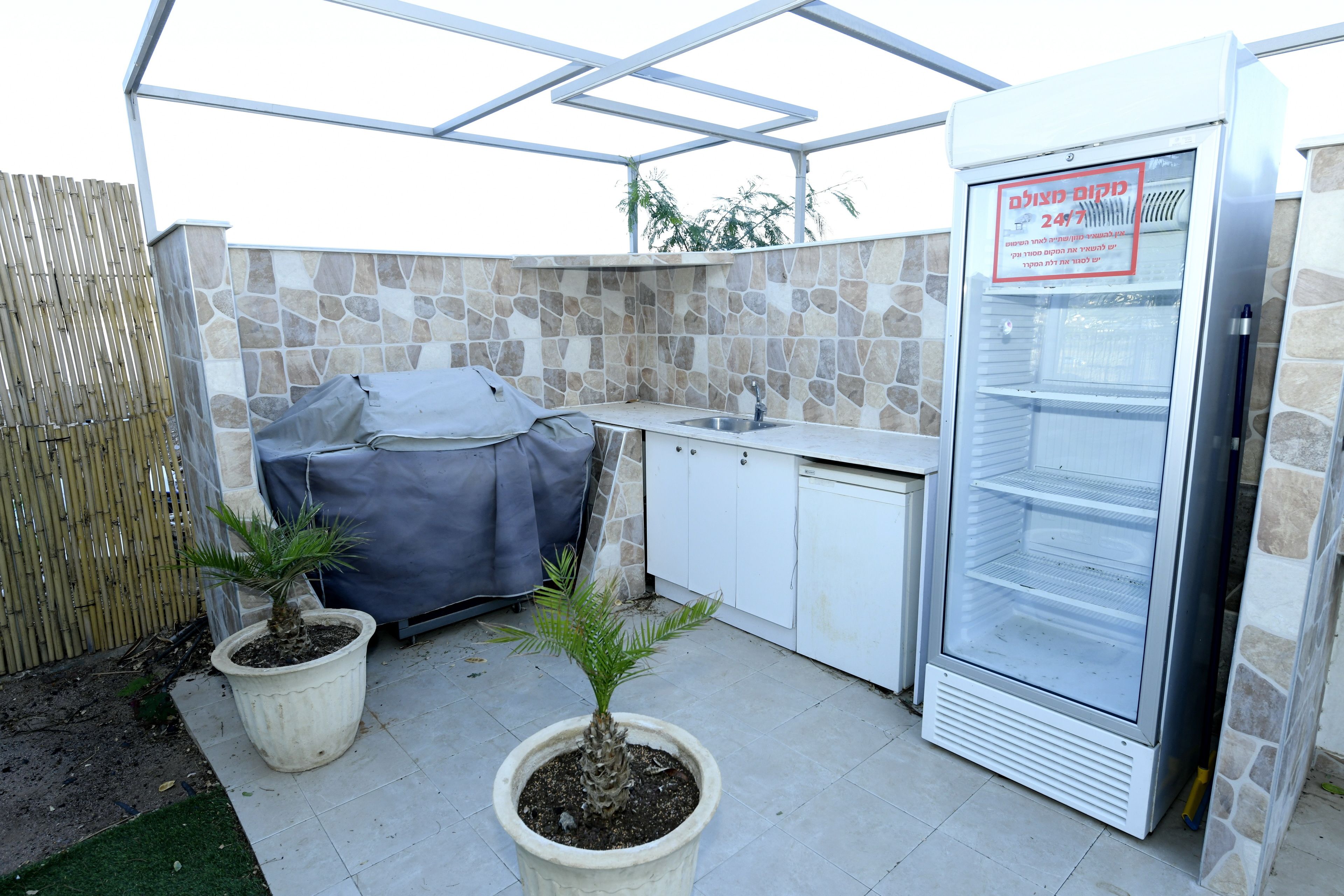 Un área de cocina al aire libre con refrigerador, dos plantas en macetas y una parrilla para barbacoa.