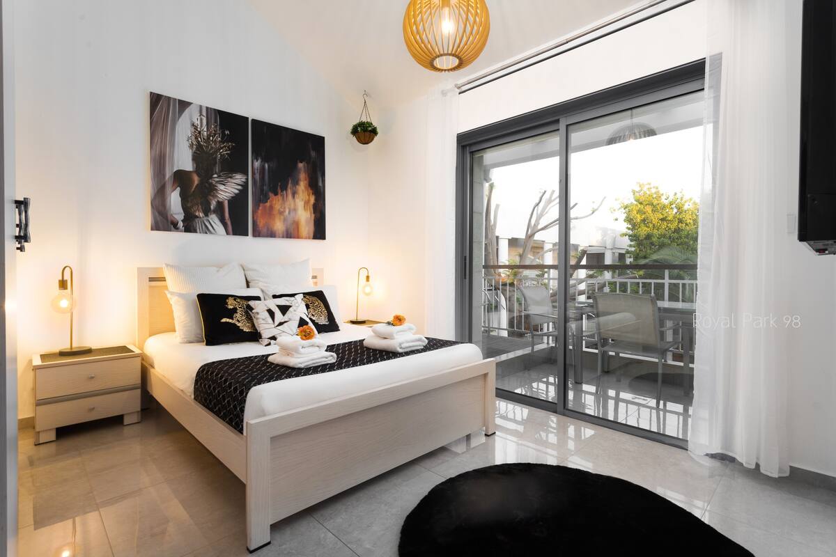 A modern bedroom with a large bed, bedside tables, and a view of the outside balcony.