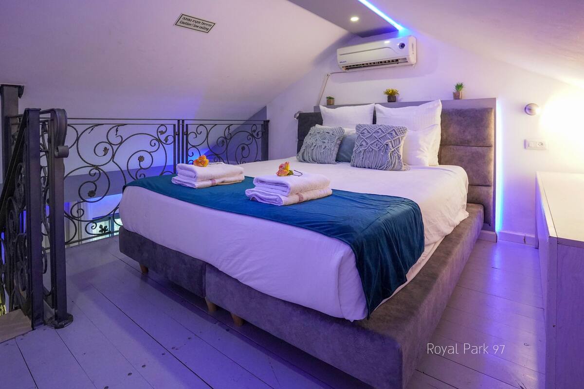 A bedroom with a bed, pillows, a bedside table, and an air conditioning unit.