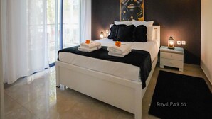 A modern bedroom with a large bed, white bedding, a black throw, and two bedside lamps.